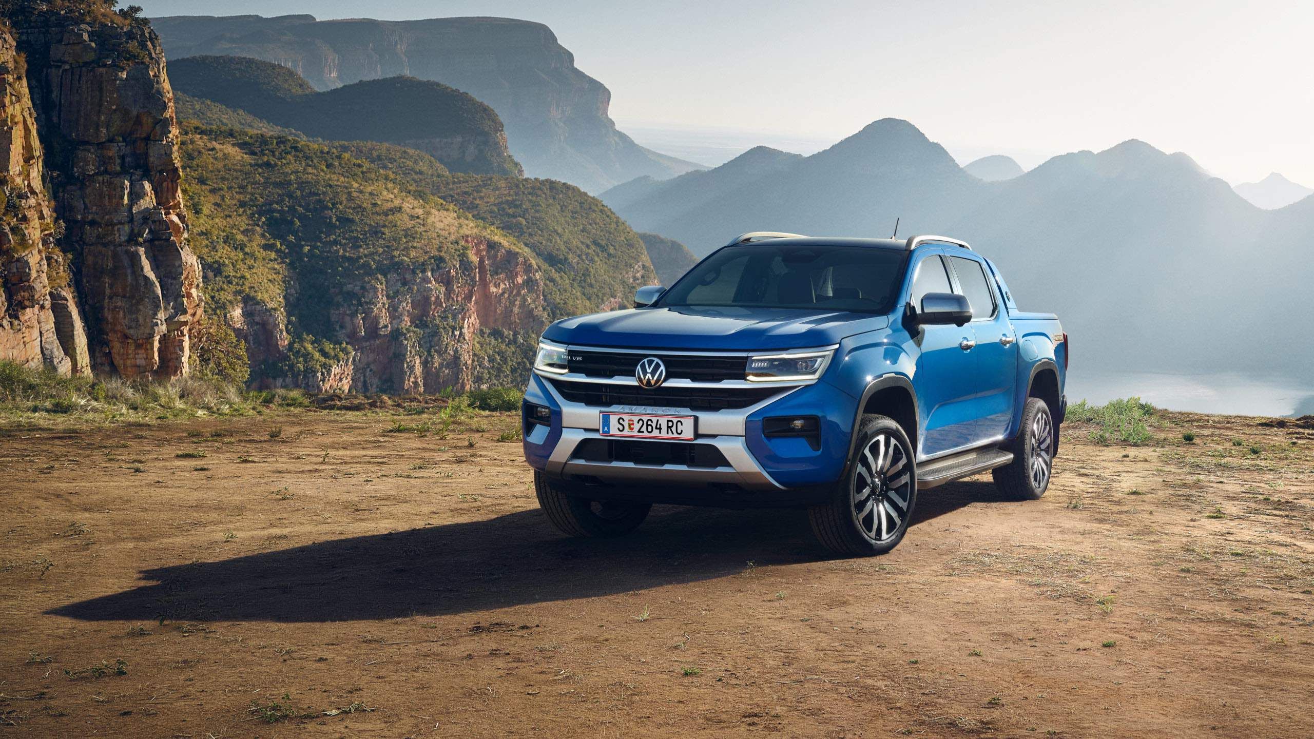 Ein VW Amarok Aventura steht an einer Klippe mit Felsen, Bergen und dem Meer im Hintergrund